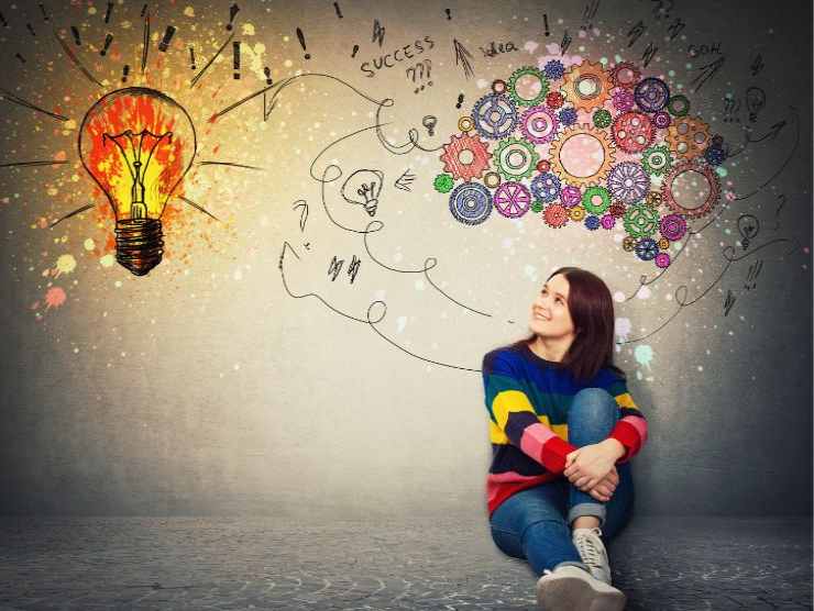 donna seduta sul pavimento e alle sue spalle una parete con una grafica che rappresenta un cervello e una lampadina