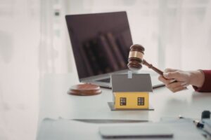 martelletto da banditore che colpisce una casa in miniatura su una scrivania con un computer portatile